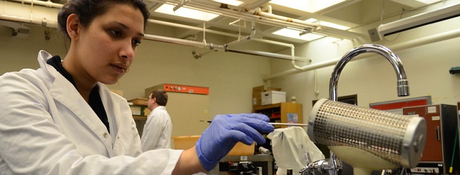 Student in lab coat and gloves putting sample into machine